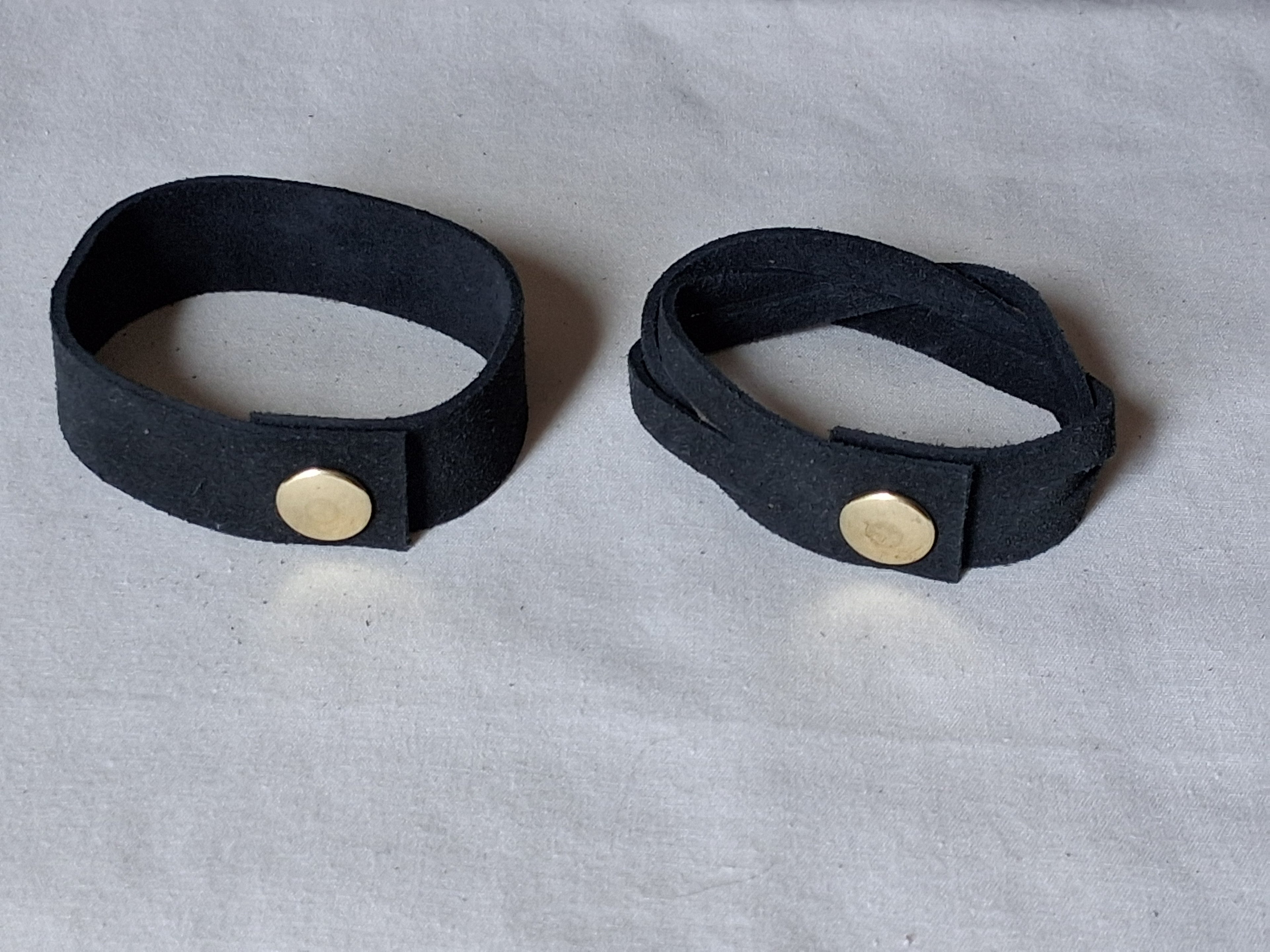 Two black leather cuffs with gold buttons on a gray background